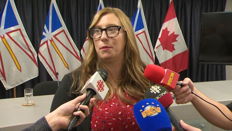 A woman with blonde hair and glasses speaks with the media.