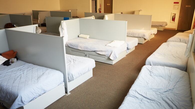 A series of beds with white sheets are pictured in a shelter.