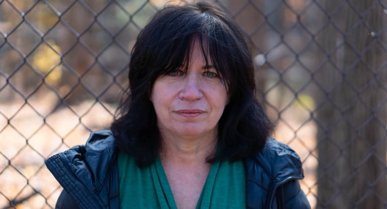 A woman is pictured standing in front of a chain link fence.