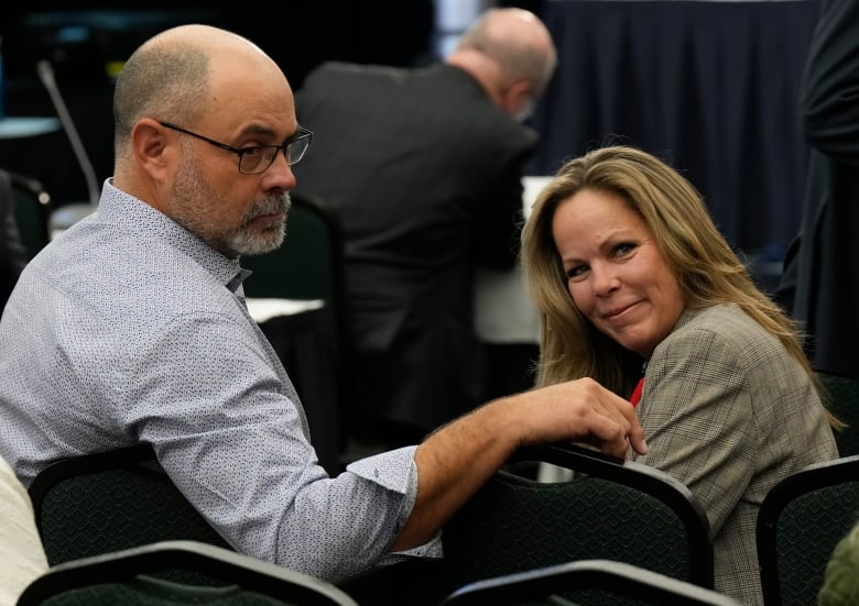 A man and woman look behind them while seated in a meeting room.