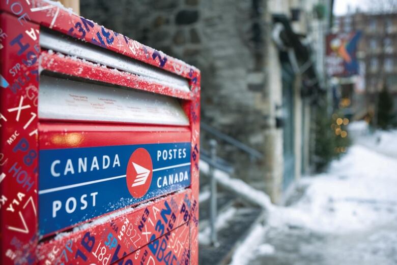 A close up of a Canada Post mailbox is seen along a wintery street.