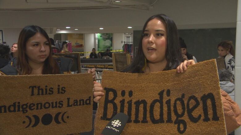 Two women hold up doormats.