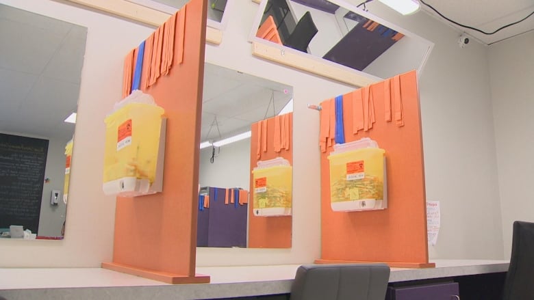 A desk with mirrors and orange dividers with sharps bins on the dividers.