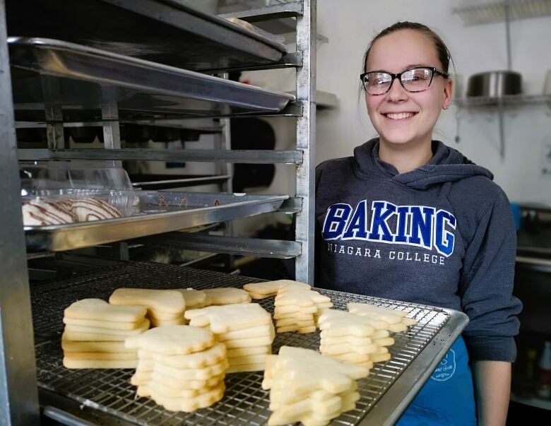 Woman poses behind undecorated cookies in Christmas shapes like trees and stockings.