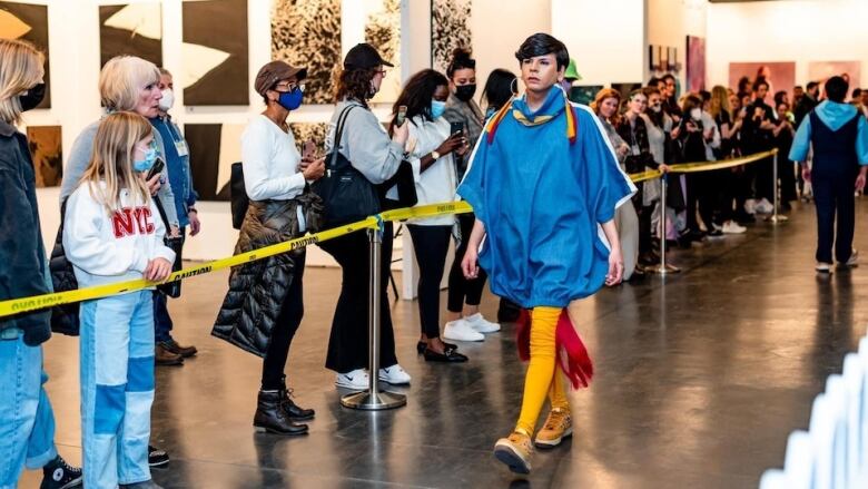 A person with a blue sweater and yellow pants walking down a catwalk.