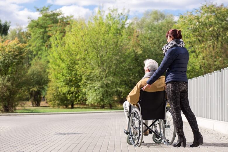 A caregiver helps an elderly man in a wheelchair, at a park