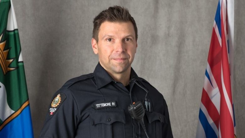 Constable Wade Tittemore stands between provincial and Canadian flags in a file photo for the Nelson Police Department. 