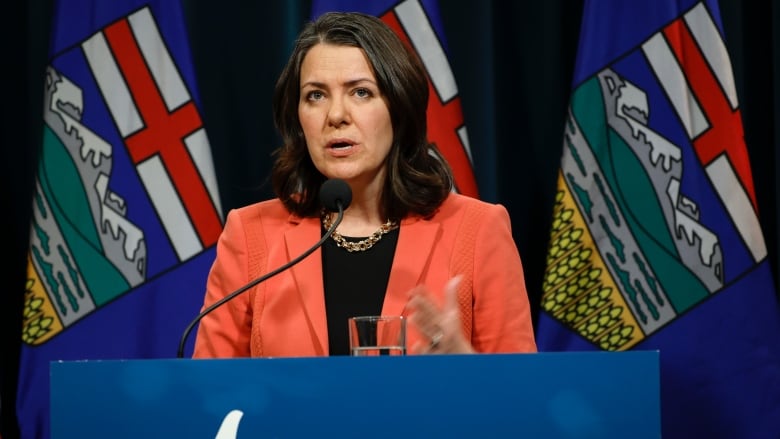 Alberta Premier Danielle Smith speaks behind a lectern bearing the provincial logo.