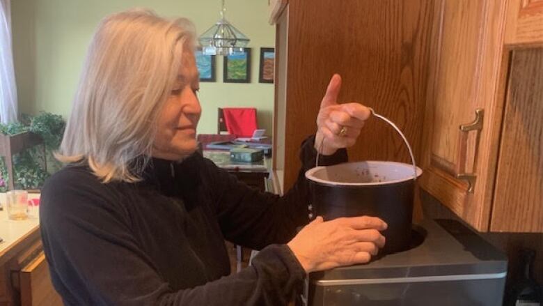 A woman stands in her kitchen and uses a FoodCycler device, which grinds down food waste and turns it into a soil amendment.