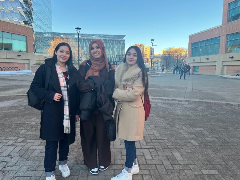 Three young women stand on a university campus. 