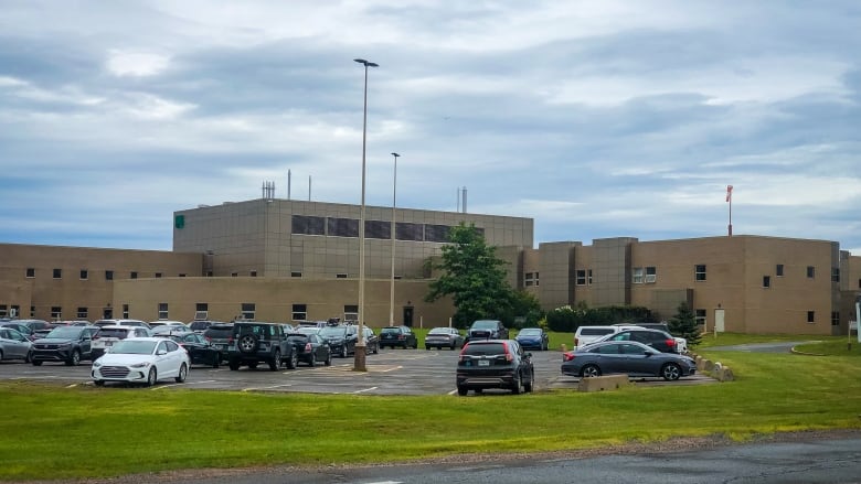 A view of a hospital, with a parking lot full of cars next to it.