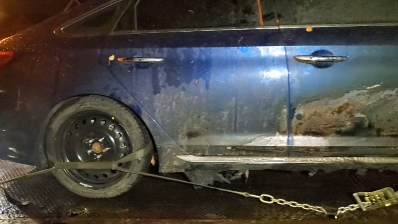 A badly burned blue car is strapped to the bed of a tow truck.