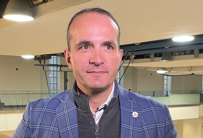 A man in a checkered jacket poses for a photograph with a gymnasium in the background.