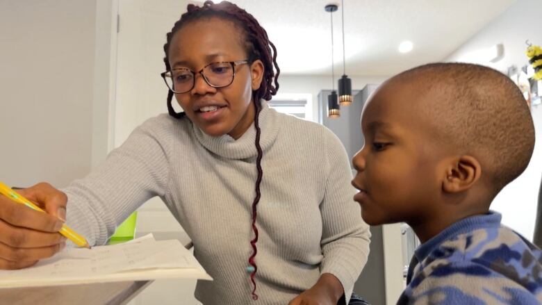 Chinwe Achebe is pictured going through a workbook with her young son at her kitchen table in southeast Calgary. 