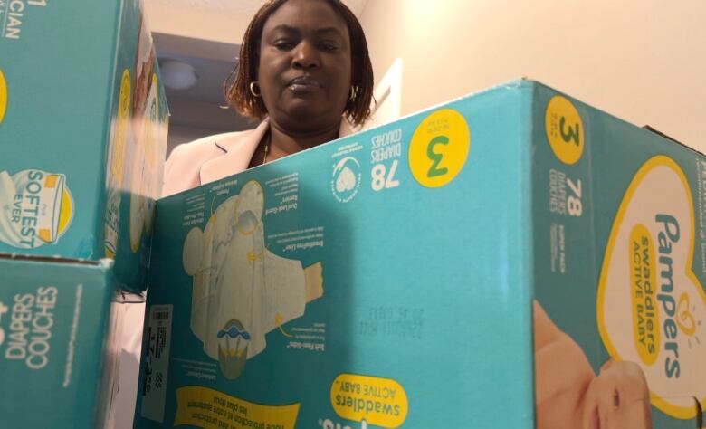 Clare Jagunna stands behind stacks of diaper boxes at her home.