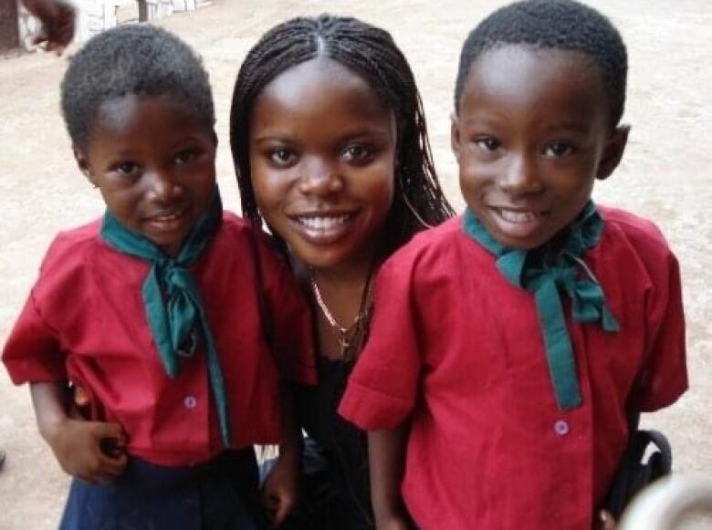 Young Black woman crouching to pose with two small children in school uniforms.