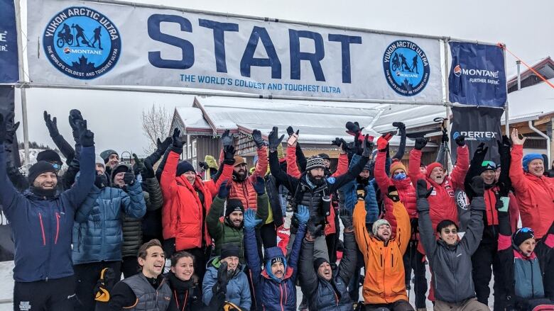 Several athletes are smiling, with their hands up in the air as they are cheering in front of the start line. 