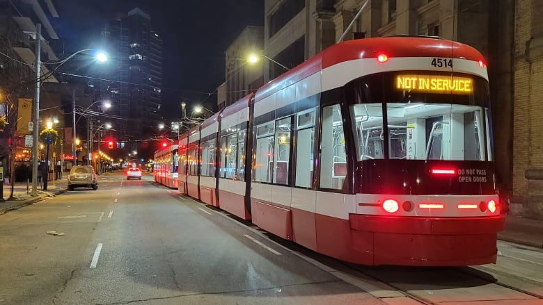 A streetcar with a 'not in service sign' is stopped in the street at night.