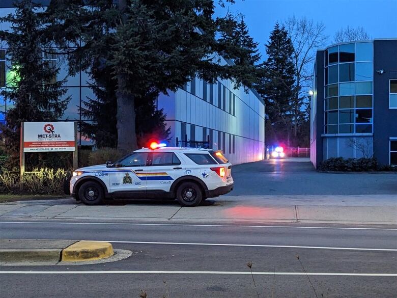 Two SUVs in RCMP livery are parked in an industrial area with their lights flashing.