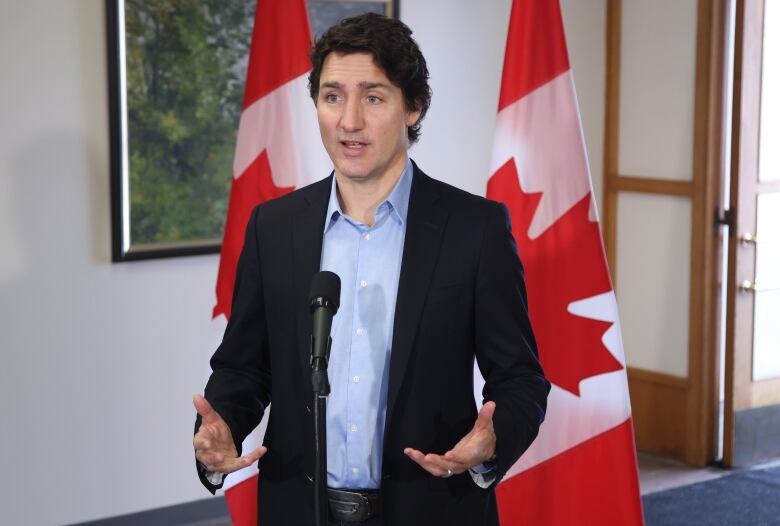 A man speaks at a microphone, flanked by two Canadian flags.