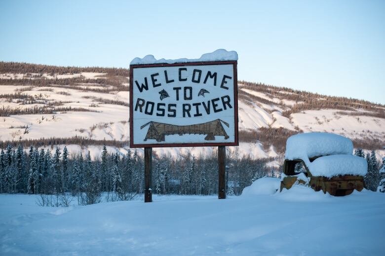 A welcome sign for the community of Ross River, Yukon. In the background are gently lit mountains.