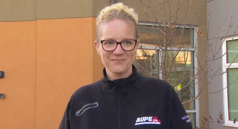 A woman wearing a black sweater, with the logo AUPE, slightly smiles beyond the camera.