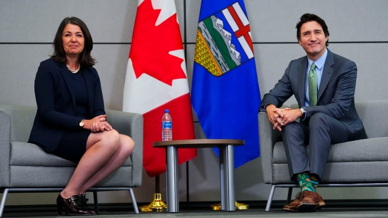 A woman with brown hair sits in a chair next to a man with black hair in a blue suit