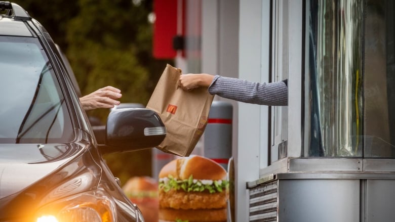 A person in a car picks up food from a drive-thru window.