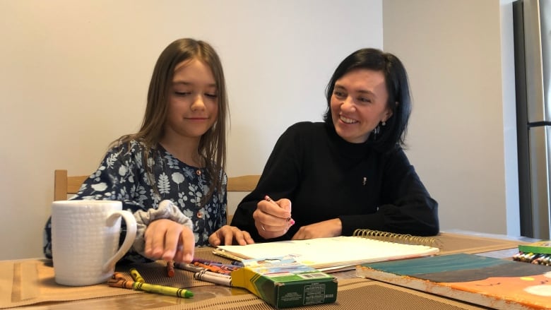 Mother and child sit at a table with crayons and paper.