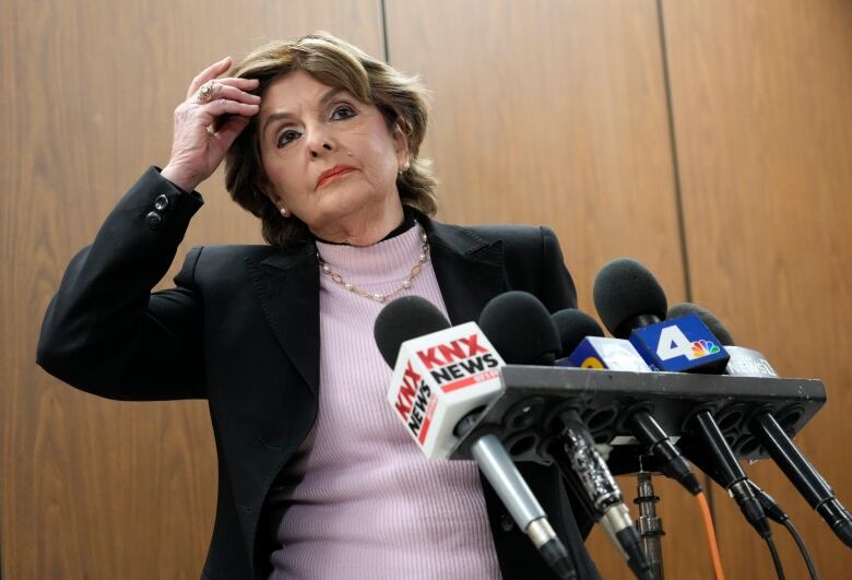 A woman in business attire stands in front of several media microphones