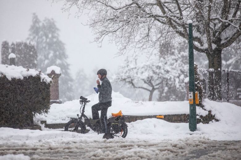 A person on a bike stops while riding down a snowy sidewalk in Vancouver.