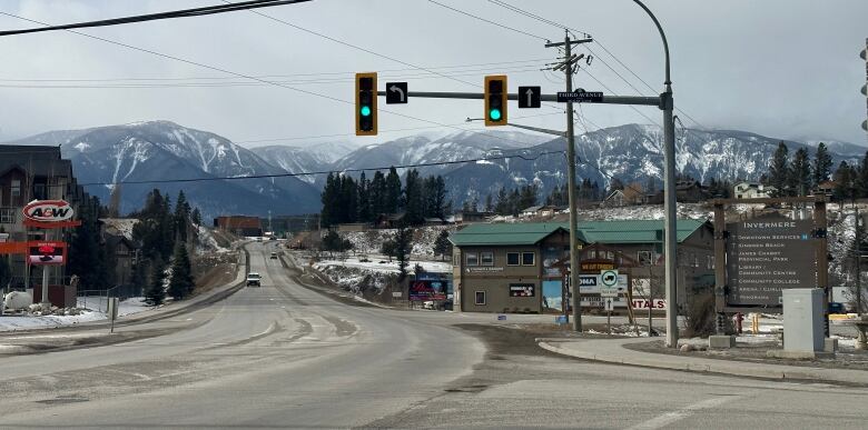 A small town street is pictured with snowy mountains in the background.