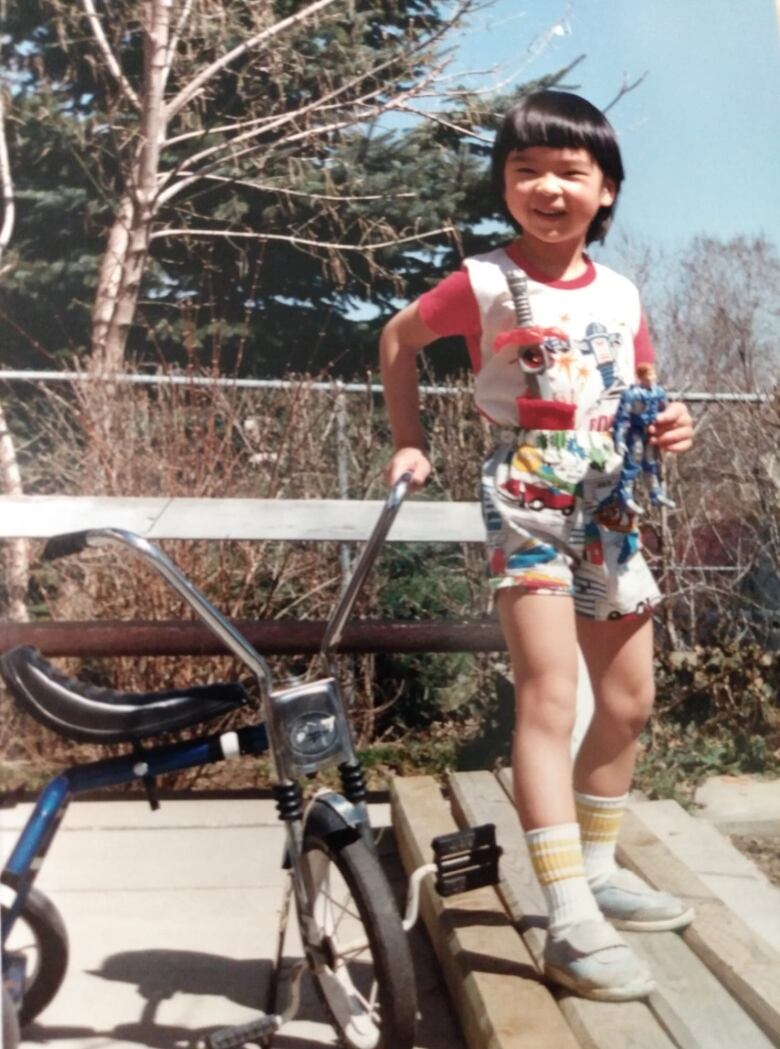 A child stands next to a tricycle.