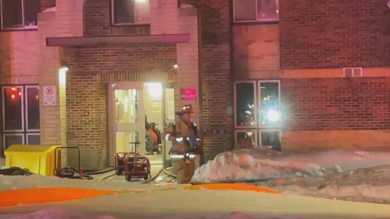 Firefighters work in and around an apartment building at night after flames were extinguished.