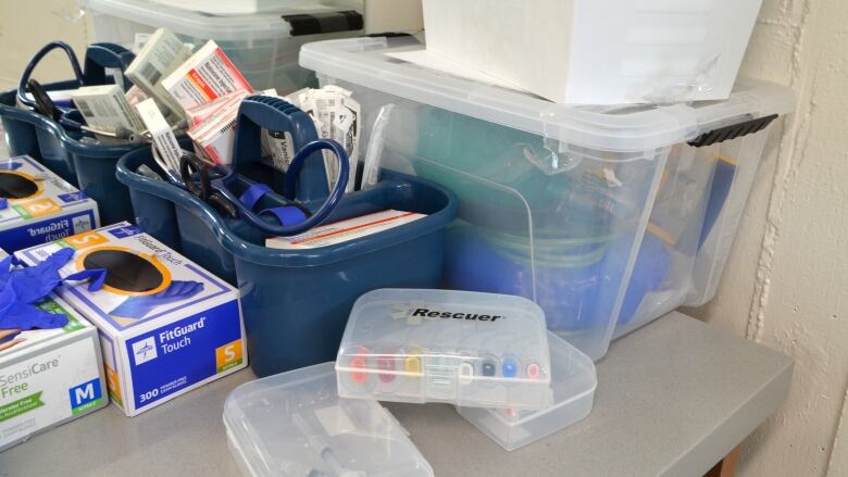 A close-up shot of medical supplies, like gloves, boxes of syringes, and plastic containers filled with other items.