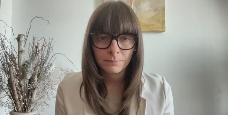 a woman in a white blazer looks into the camera. she has bangs