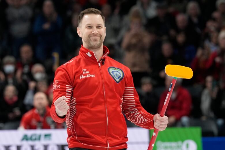 A male curling skip grins while pumping his right fist and holding a broom in his left.