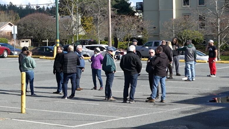 A number of people mill around a parking lot.