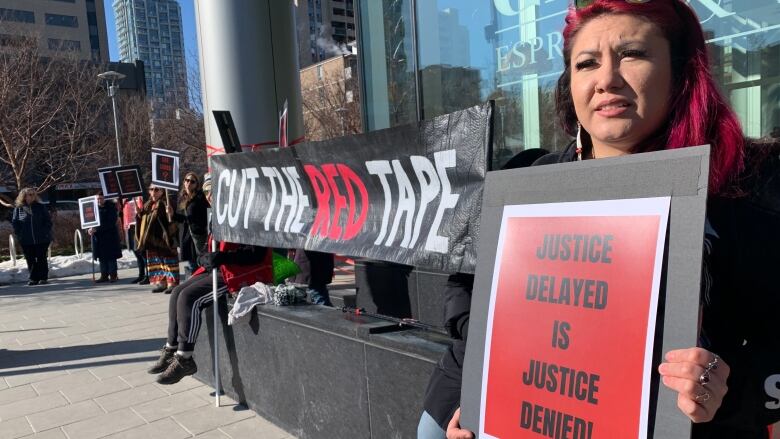 A woman with red hair holds a red sign bearing the words, 