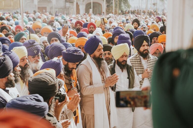 Hundreds of men wearing turbans prey outside a building in India