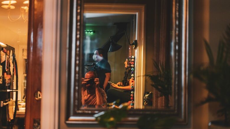 Creators Pearly Pouponneau and Quest stand facing a mirror with a camera to capture behind the scenes shots of their video. 