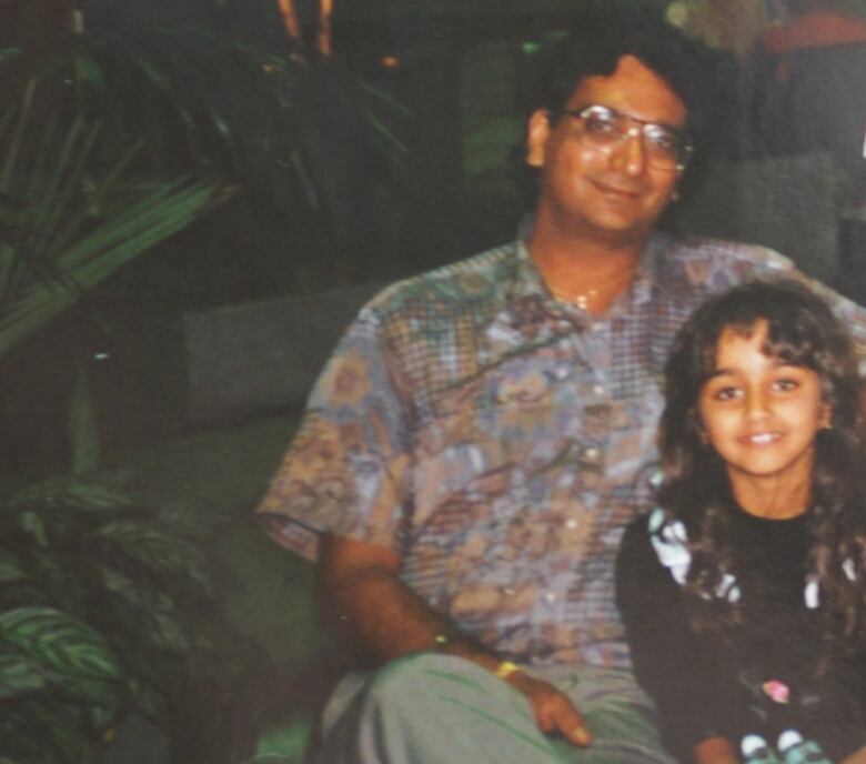 A man sits outside with an arm around his daughter in an old family photo. 