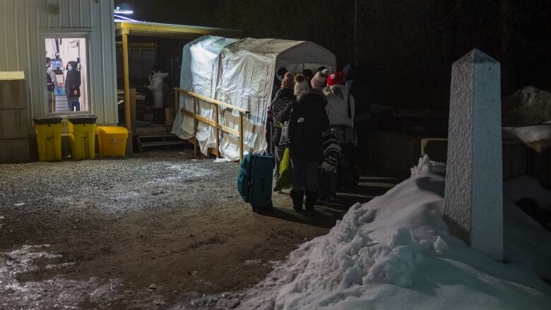 Asylum seekers line up at the RCMP's temporary post on Roxham Road. A white marker delimitating the border is seen on the right.