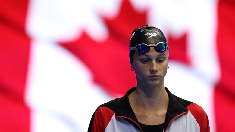 A women's swimmer is seen with a large Canadian flag as the background.