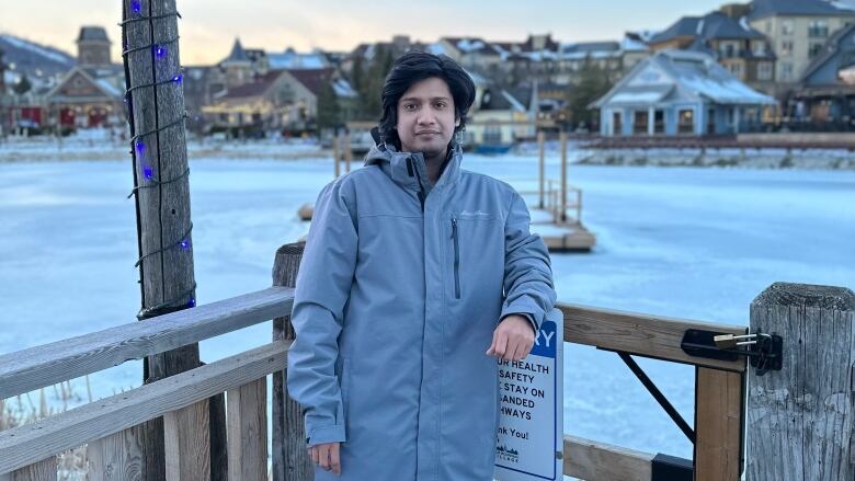 A man wearing a winter jacket standing in front of a frozen body of water. 