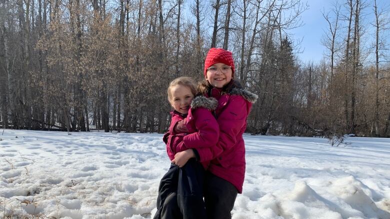 Two young girls smile at the camera in the sunny, snowy river valley.