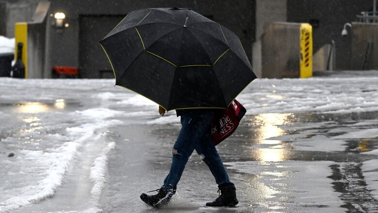 Someone with an open umbrella walks through a puddle as freezing rain falls.