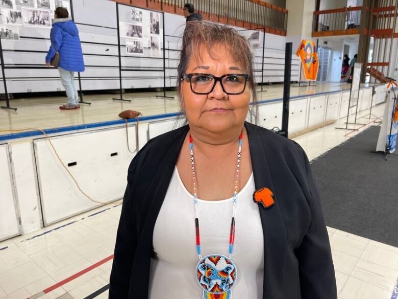 A woman with brown hair and black glasses stands in a gymnasium.