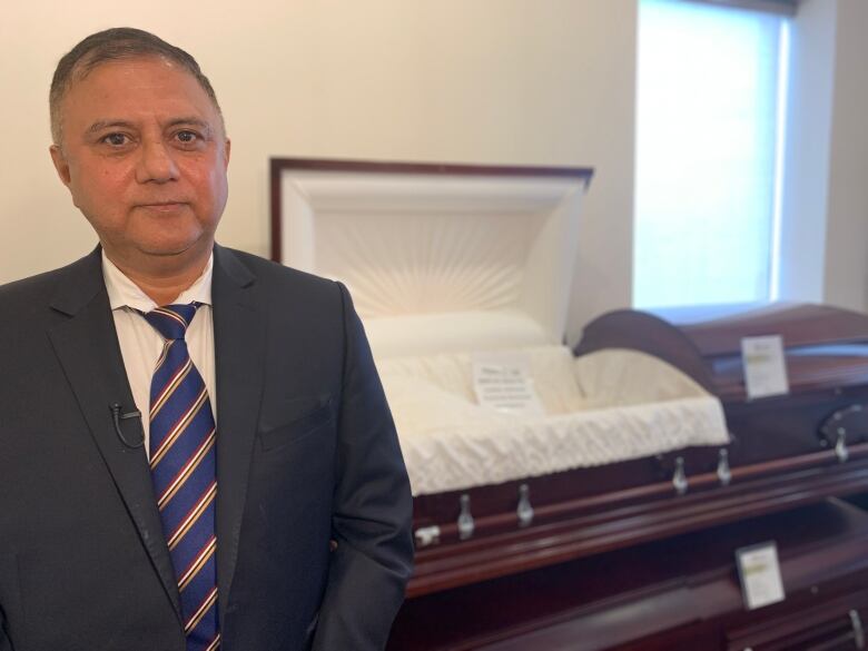 Harminder Hamsi stands in front of a funeral coffin at Lotus Funeral and Cremation Centre's selection room. 