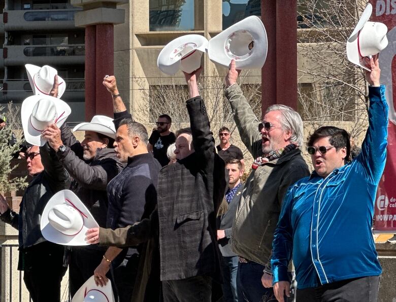 A group of people hold white hats in the air.